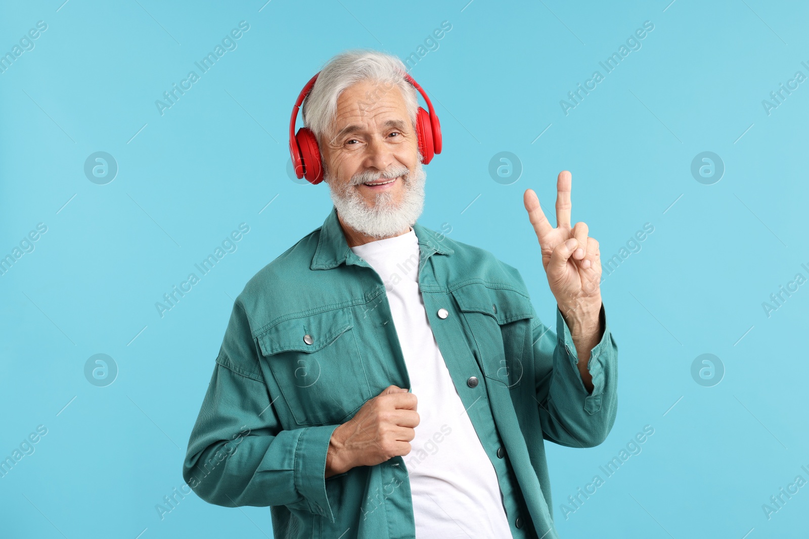 Elderly man in headphones showing peace sign on light blue background Photo of Elderly man in headphones showing peace sign on light blue background