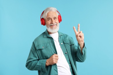 Photo of Elderly man in headphones showing peace sign on light blue background