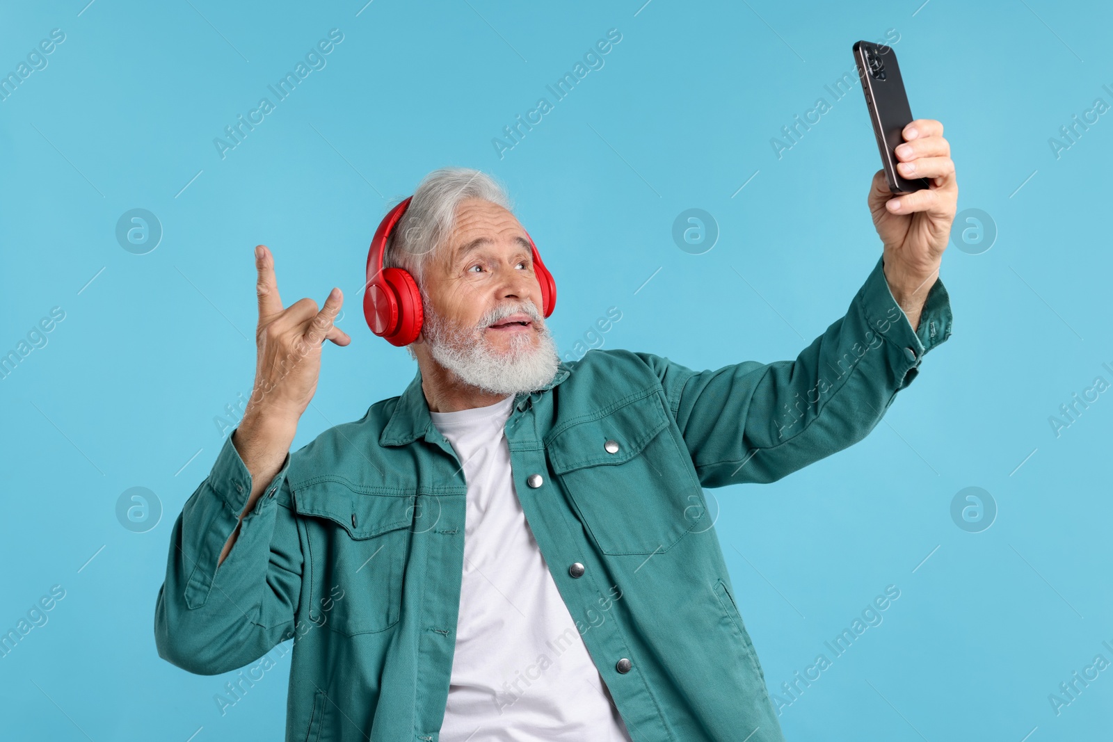 Elderly man in headphones taking selfie on light blue background Photo of Elderly man in headphones taking selfie on light blue background