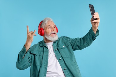 Photo of Elderly man in headphones taking selfie on light blue background