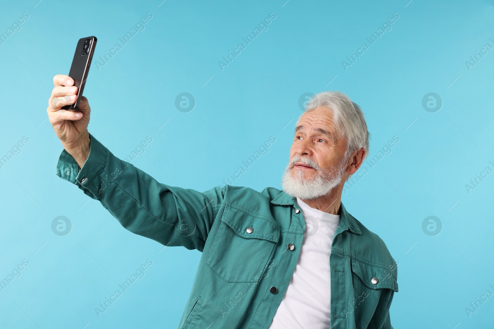 Elderly man taking selfie on light blue background Photo of Elderly man taking selfie on light blue background