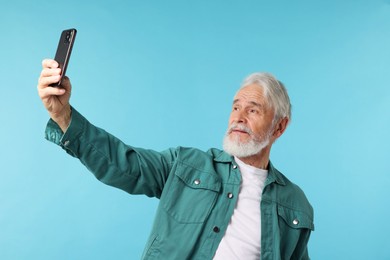 Photo of Elderly man taking selfie on light blue background