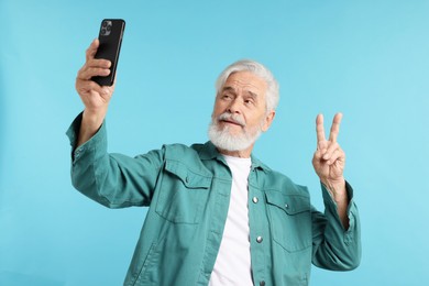 Photo of Elderly man showing peace sign while taking selfie on light blue background