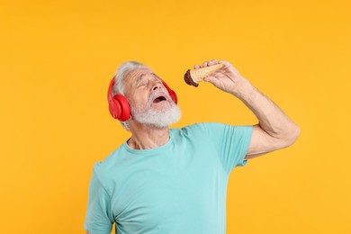 Photo of Elderly man in headphones with ice cream on orange background