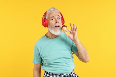 Photo of Elderly man in headphones with ice cream on orange background