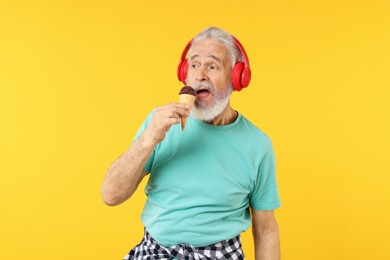 Photo of Elderly man in headphones with ice cream on orange background