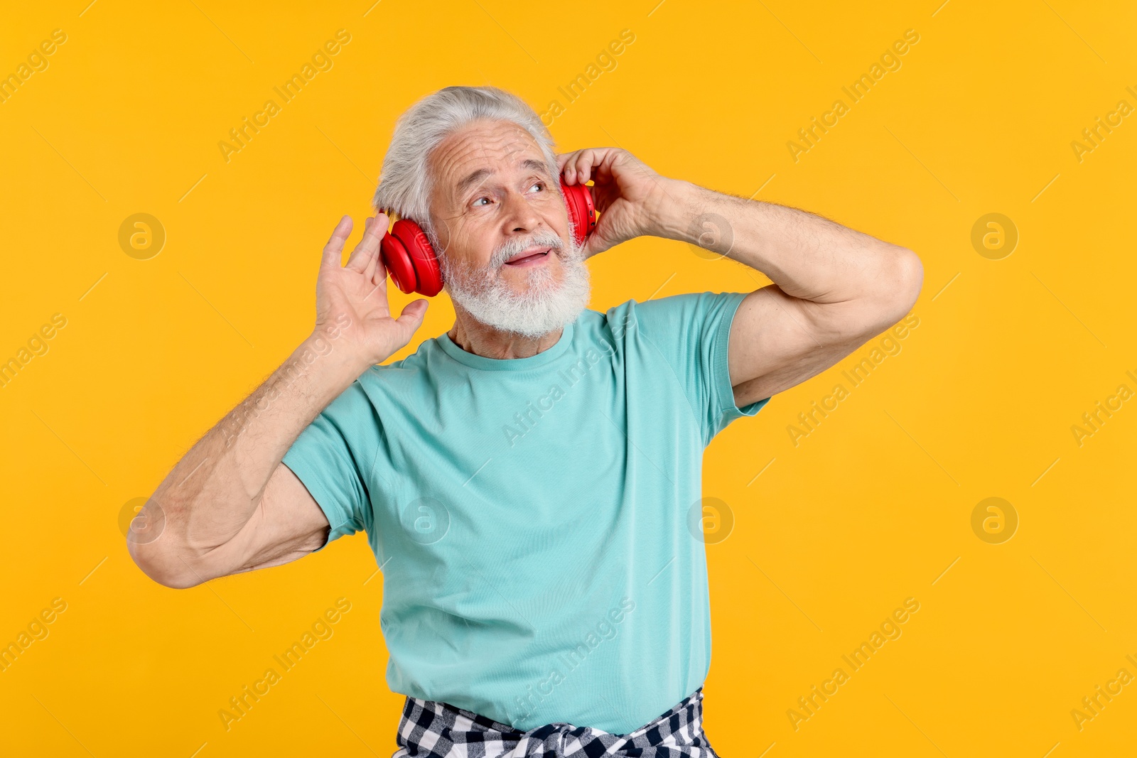 Elderly man with headphones on orange background Photo of Elderly man with headphones on orange background