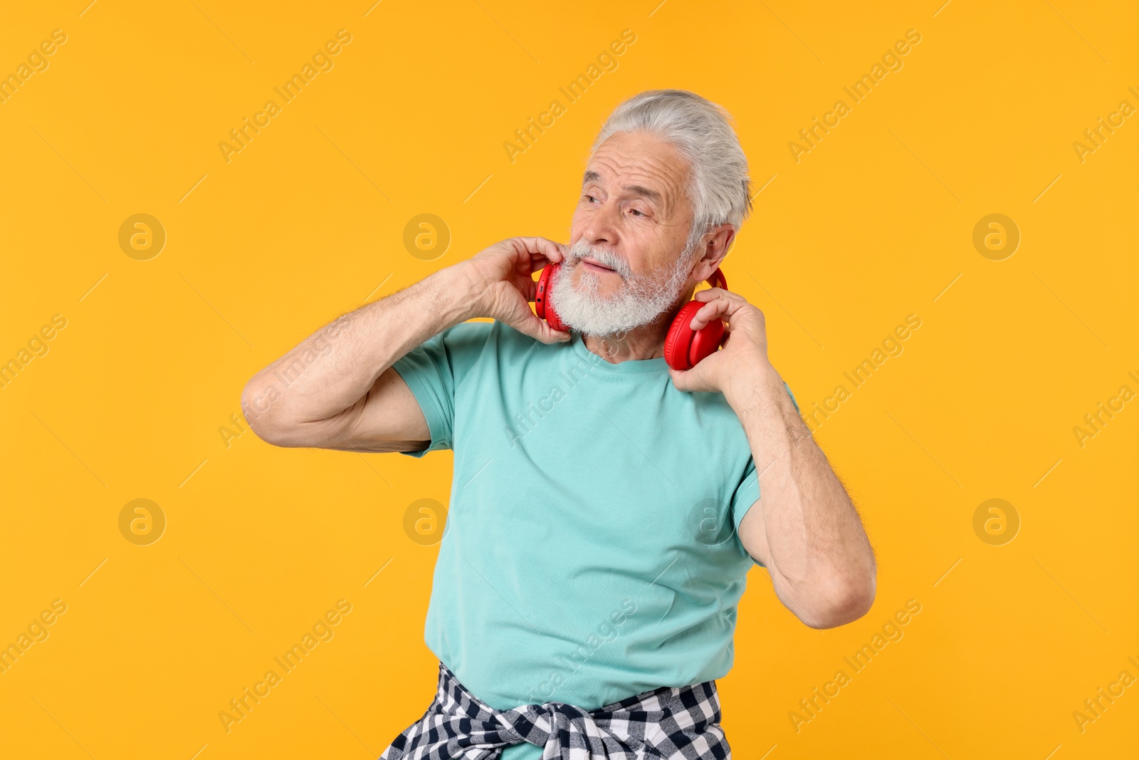 Elderly man with headphones on orange background Photo of Elderly man with headphones on orange background