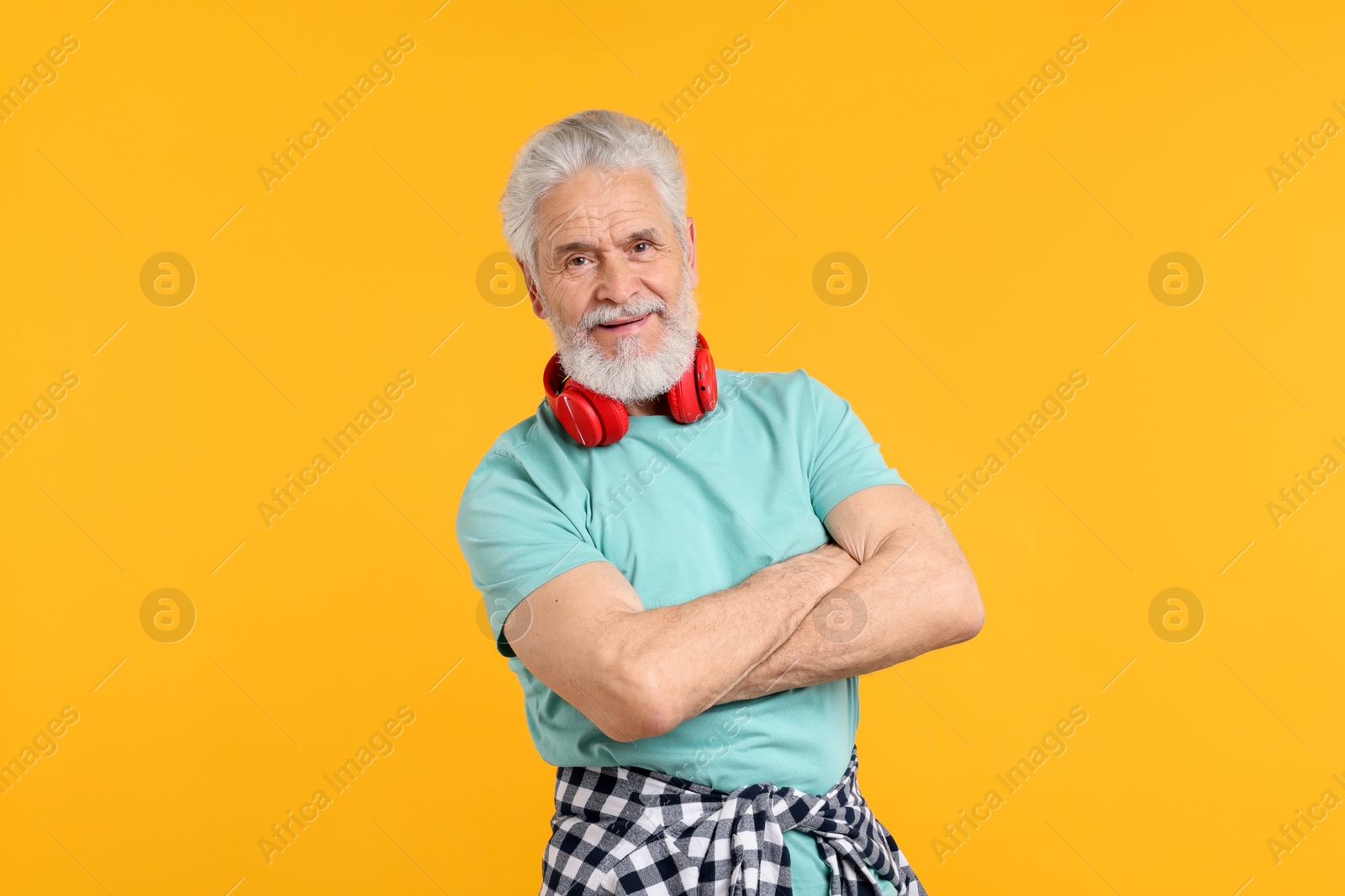 Elderly man with headphones on orange background Photo of Elderly man with headphones on orange background