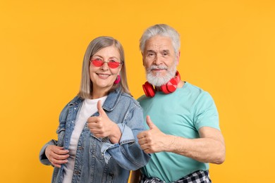 Photo of Senior couple in stylish outfits showing thumbs up on orange background