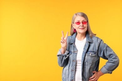 Photo of Senior woman in stylish outfit showing v-sign on orange background, space for text