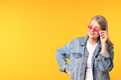 Photo of Senior woman wearing stylish sunglasses on orange background, space for text