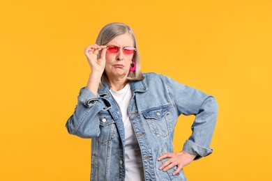 Photo of Senior woman wearing stylish sunglasses on orange background