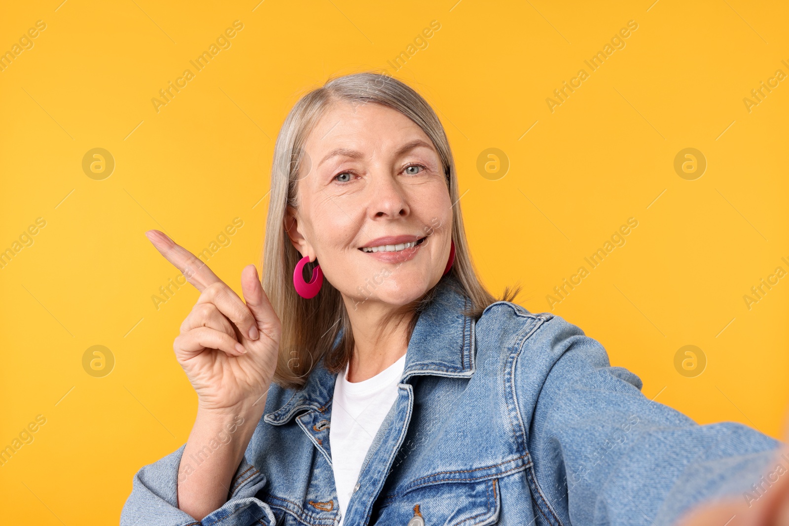 Senior woman in stylish outfit taking selfie on orange background Photo of Senior woman in stylish outfit taking selfie on orange background