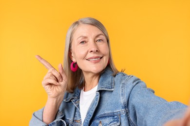 Photo of Senior woman in stylish outfit taking selfie on orange background