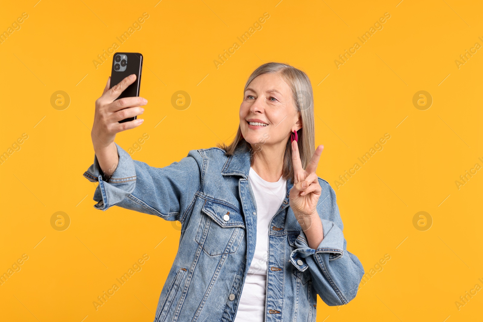 Senior woman in stylish outfit taking selfie on orange background Photo of Senior woman in stylish outfit taking selfie on orange background