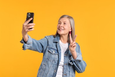 Photo of Senior woman in stylish outfit taking selfie on orange background