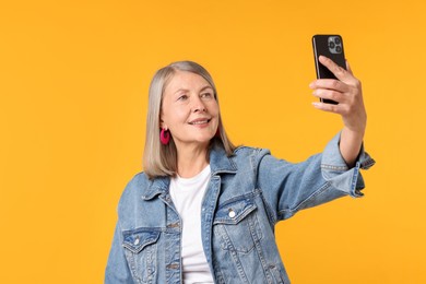 Photo of Senior woman in stylish outfit taking selfie on orange background