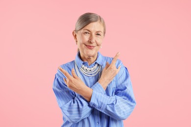 Photo of Senior woman wearing elegant pearl jewelry and making rock gesture on pink background