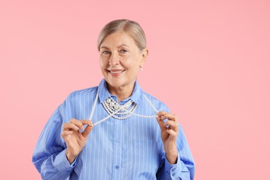 Photo of Senior woman wearing elegant pearl jewelry on pink background, space for text