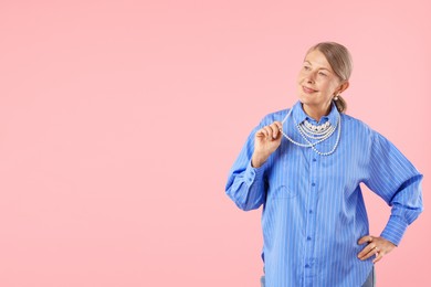 Photo of Senior woman wearing elegant pearl jewelry on pink background, space for text