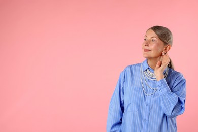 Photo of Senior woman wearing elegant pearl jewelry on pink background, space for text