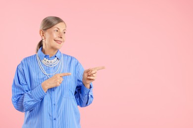 Photo of Senior woman wearing elegant pearl jewelry on pink background, space for text