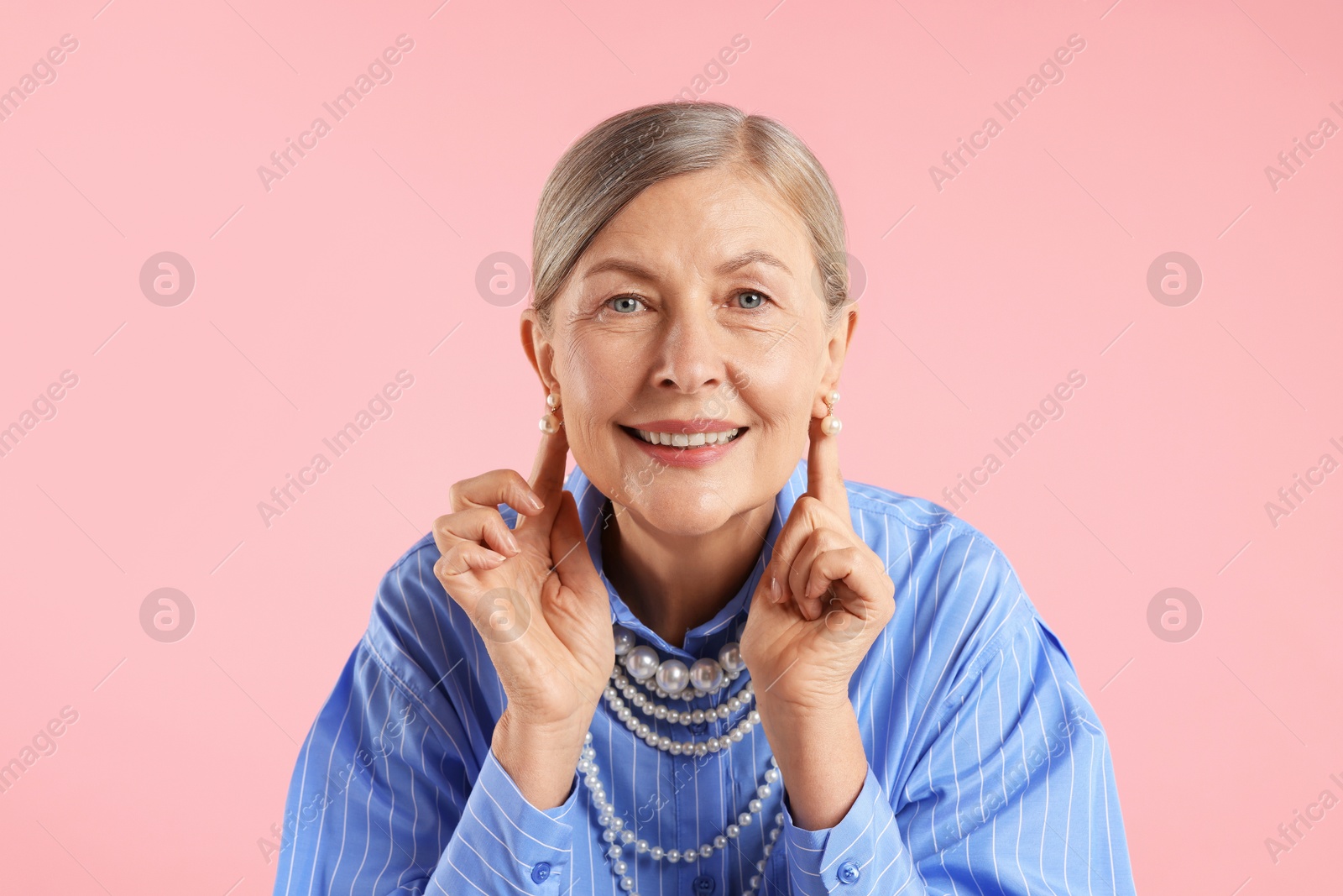 Senior woman wearing elegant pearl jewelry on pink background Photo of Senior woman wearing elegant pearl jewelry on pink background