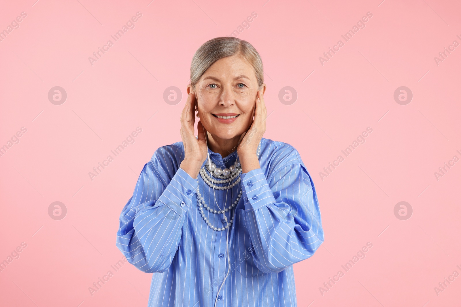 Senior woman in earphones listening to music on pink background Photo of Senior woman in earphones listening to music on pink background