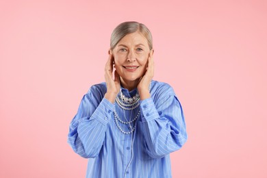 Photo of Senior woman in earphones listening to music on pink background