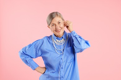 Photo of Senior woman in earphones listening to music on pink background