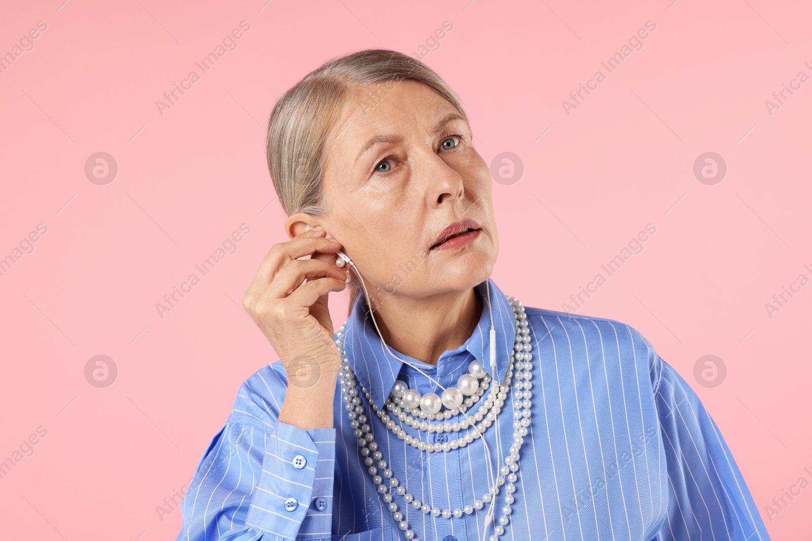 Senior woman in earphones listening to music on pink background Photo of Senior woman in earphones listening to music on pink background