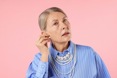 Photo of Senior woman in earphones listening to music on pink background