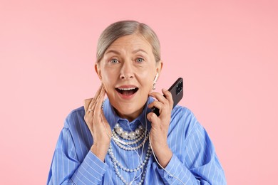 Photo of Senior woman in earphones listening to music on pink background