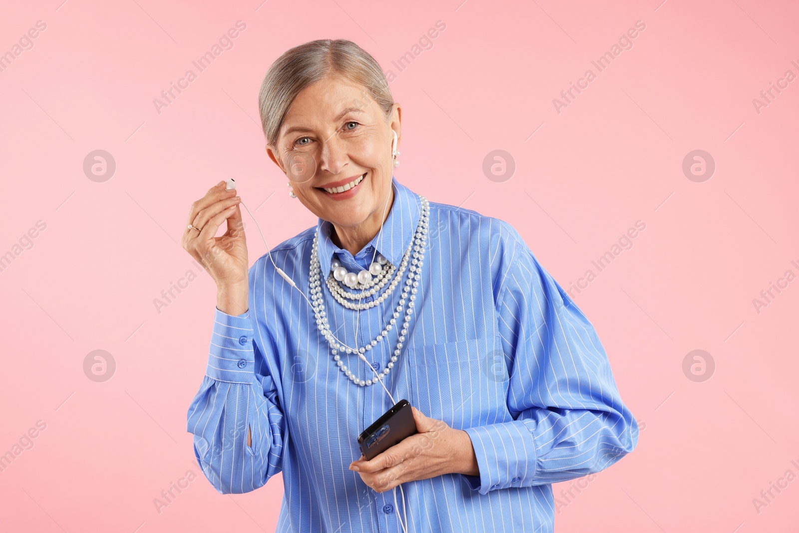 Senior woman in earphones listening to music on pink background Photo of Senior woman in earphones listening to music on pink background