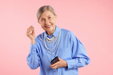 Photo of Senior woman in earphones listening to music on pink background