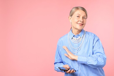 Photo of Senior woman in earphones listening to music on pink background, space for text