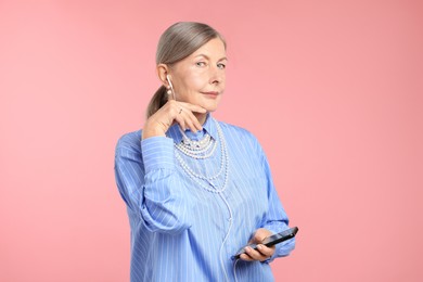 Photo of Senior woman in earphones listening to music on pink background