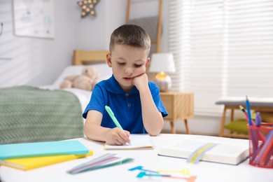 Photo of Dyslexia. Little boy writing at table indoors