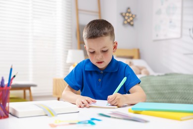 Photo of Dyslexia. Little boy writing at table indoors