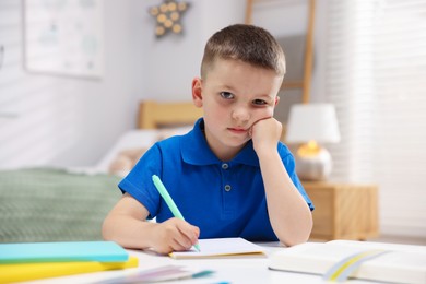 Photo of Dyslexia. Upset little boy writing at table indoors