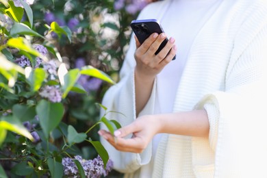 Photo of Woman using plant recognition application on smartphone outdoors, closeup