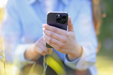 Photo of Woman using plant recognition application on smartphone outdoors on sunny day, closeup