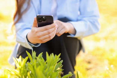 Photo of Woman using plant recognition application on smartphone outdoors on sunny day, closeup