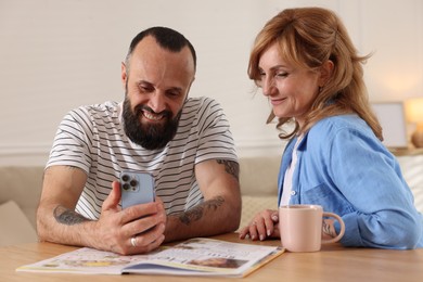 Photo of Lovely couple watching something on smartphone at wooden table indoors