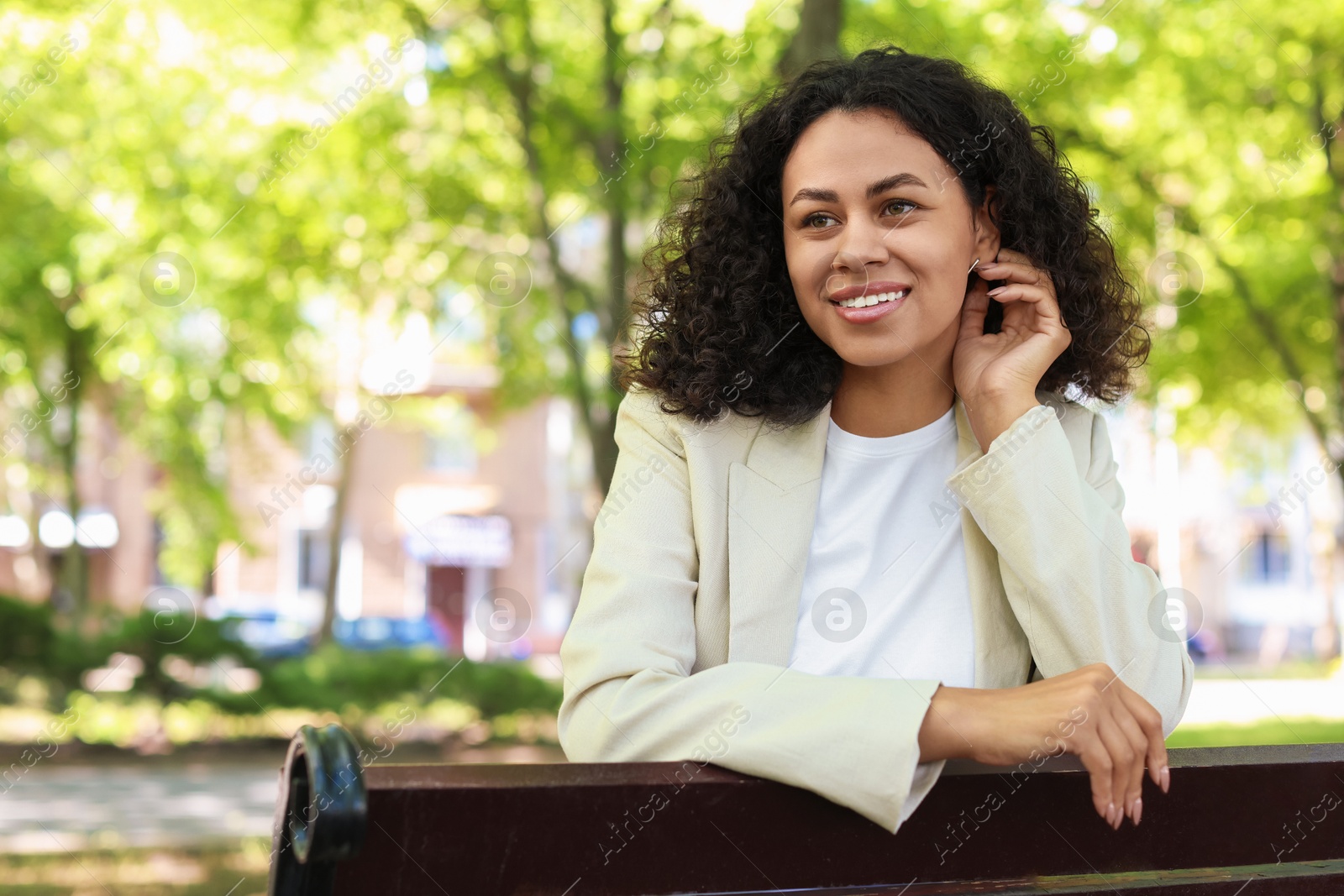 Portrait of smiling Latin American woman on bench outdoors. Space for text Photo of Portrait of smiling Latin American woman on bench outdoors. Space for text