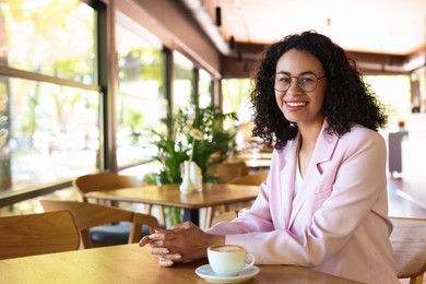 Photo of Portrait of smiling Latin American woman at table in cafe