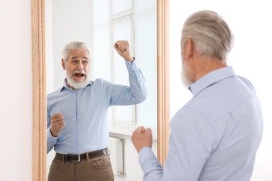 Photo of Handsome senior man looking at himself in mirror indoors