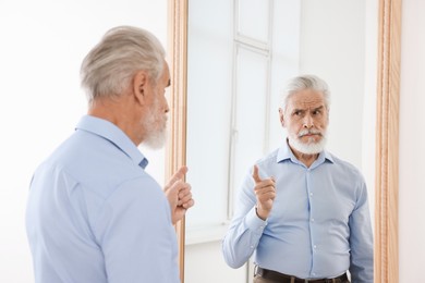 Photo of Handsome senior man looking at himself in mirror indoors