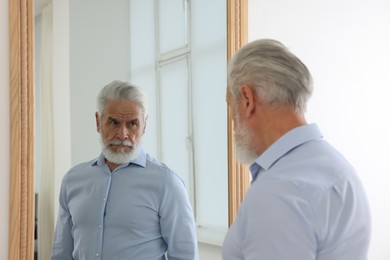 Photo of Handsome senior man looking at himself in mirror indoors